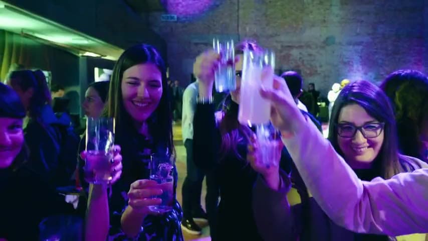 Guests toasting cocktails at the Raise the Bar conference under purple stage lighting